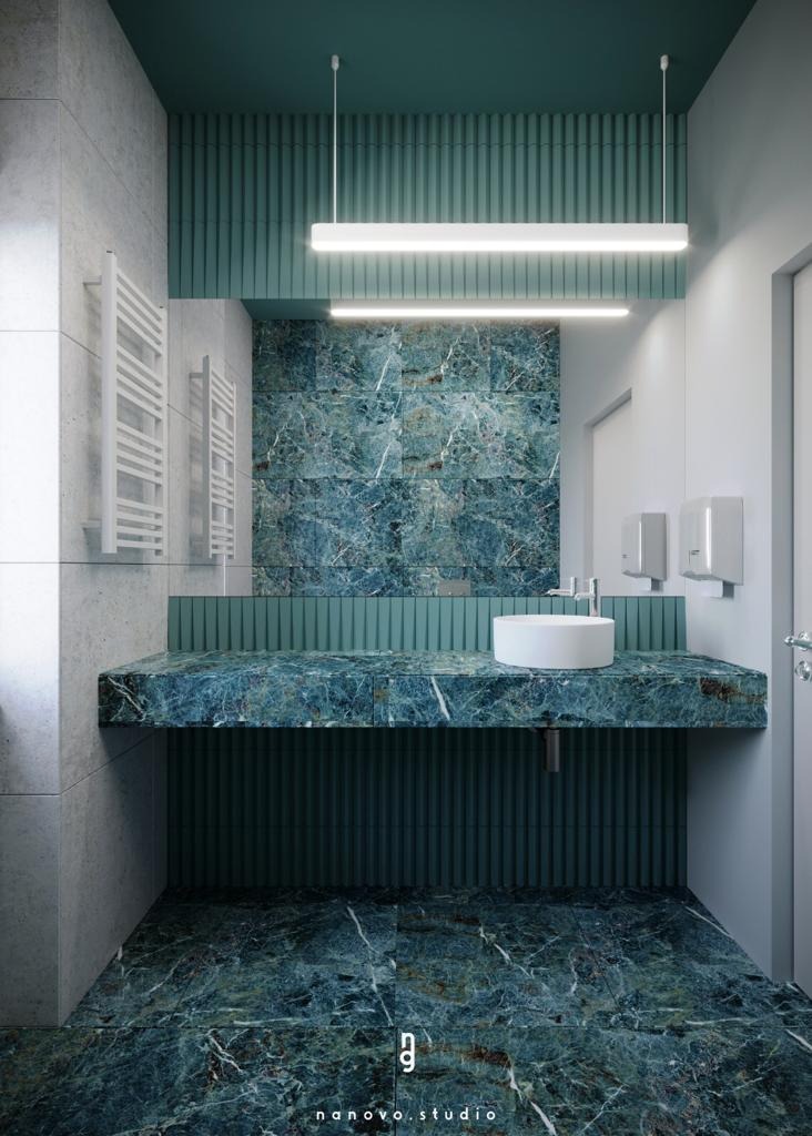 Nowoczesna łazienka z zielonym marmurem na podłodze, ścianach i blacie umywalki, oświetlona podłużnymi lampami LED, z okrągłą białą umywalką nablatową i grzejnikiem drabinkowym.