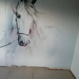 Malowidło ścienne przedstawiające białego konia z czarną uprzężą, wykonane w stylu akwareli, na ścianie w trakcie remontu, z widocznymi pozostałościami po starej podłodze.