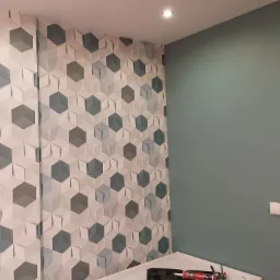 Nowoczesna ściana z trójwymiarowymi, sześciokątnymi panelami w odcieniach szarości i błękitu, kontrastująca z gładką, turkusową ścianą obok w jasnym wnętrzu.