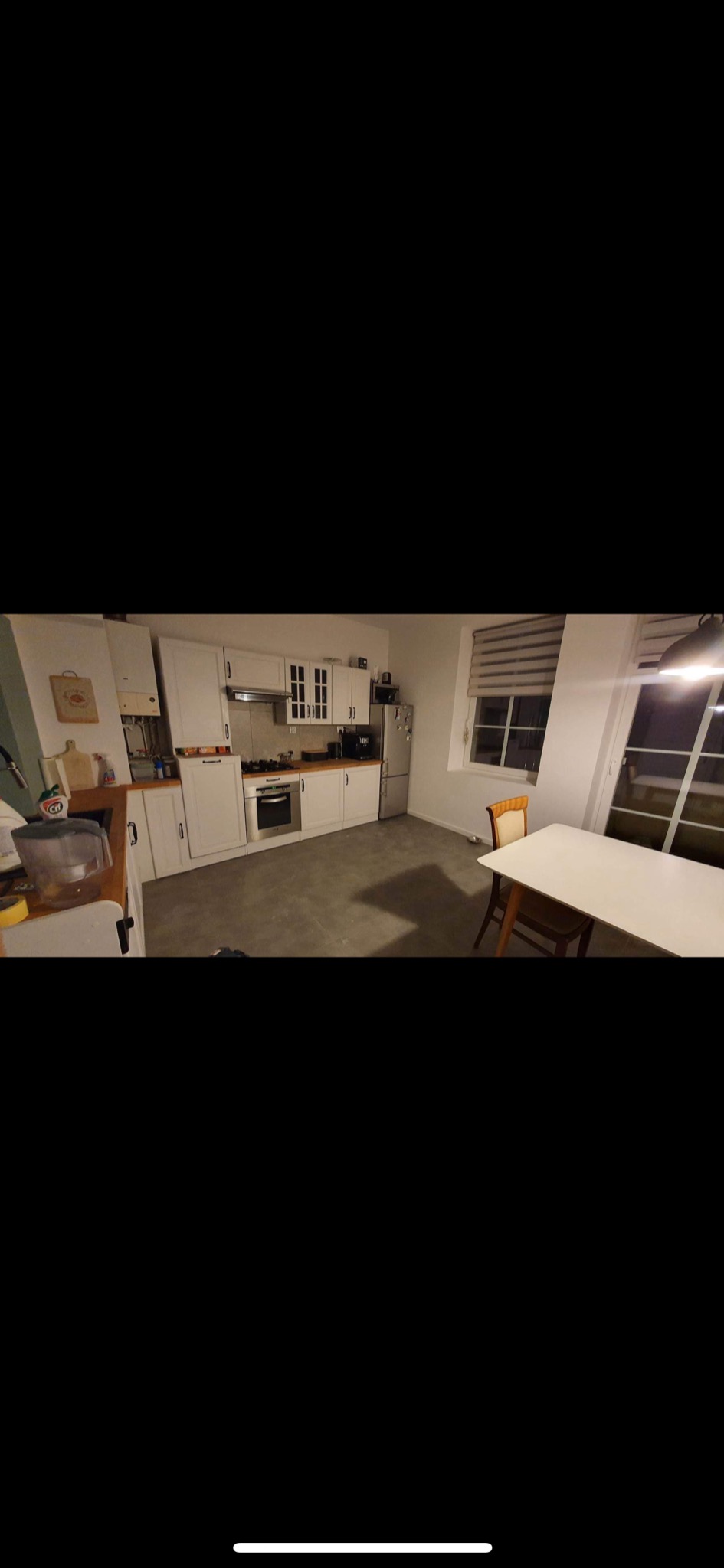 Jasna kuchnia z białymi szafkami, srebrną lodówką i stołem z krzesłami przy oknie, widok z przodu.