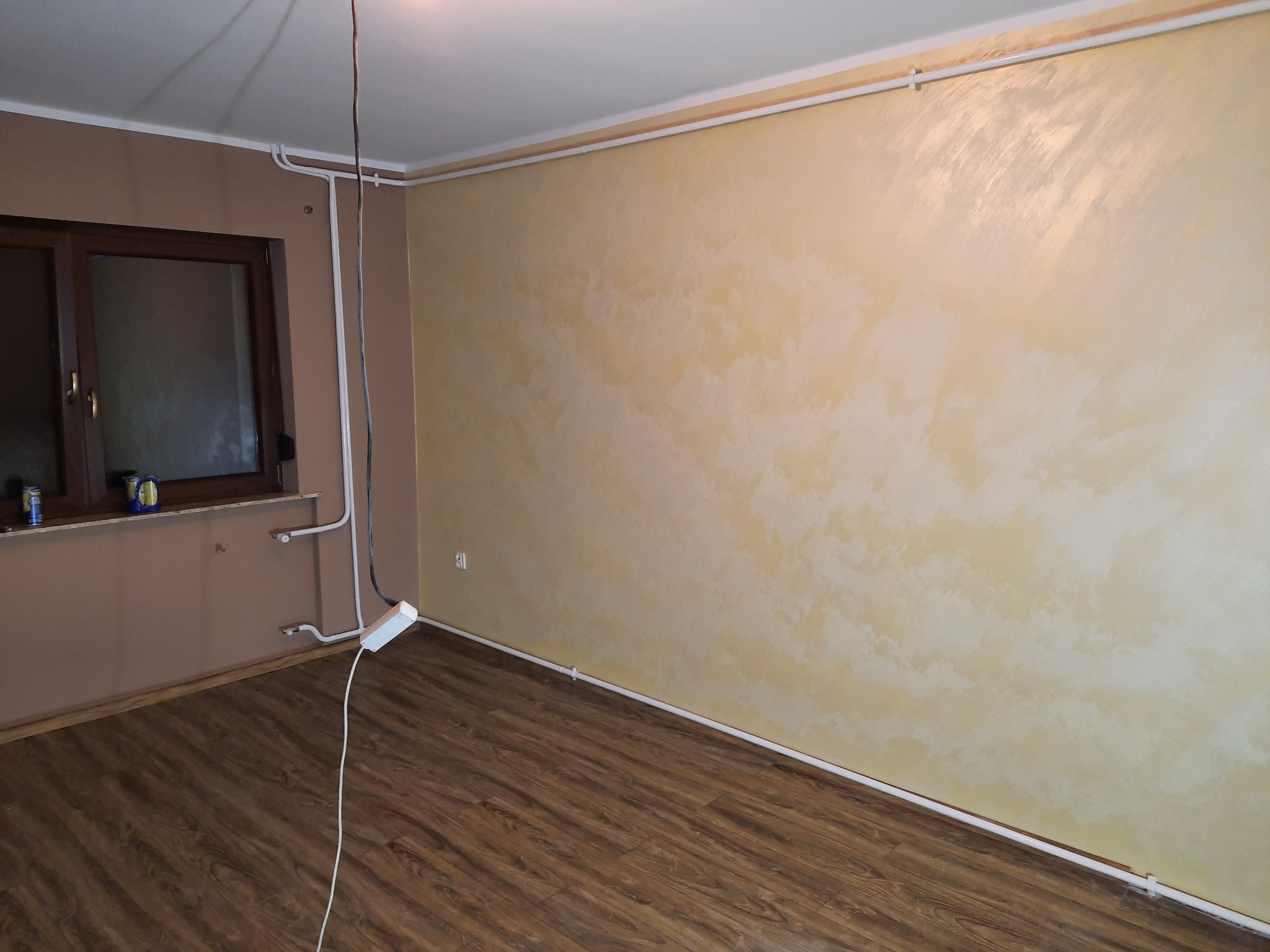 Pokój po malowaniu ścian na jasny, kremowy odcień z efektem chmur i ułożeniu podłogi z paneli imitujących drewno; widoczne listwy przypodłogowe i instalacja elektryczna.