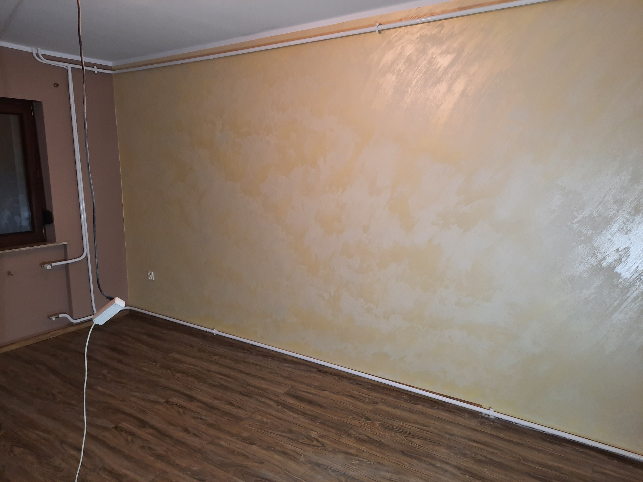 Ściana w pokoju w Dobrzycy z dekoracyjnym efektem malarskim w odcieniach beżu i bieli, widoczna instalacja elektryczna przy podłodze i suficie.