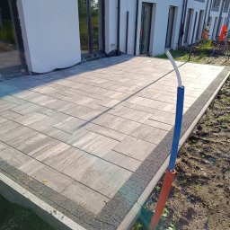 SEB-POL Sebastian Chmielarz - Ułożona kostka brukowa na tarasie domu jednorodzinnego, widoczne obrzeża i fragment instalacji. Jasne, naturalne światło.