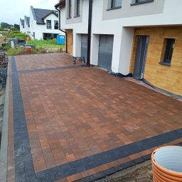 SEB-POL Sebastian Chmielarz - Ukończony podjazd z kostki brukowej w odcieniach brązu i grafitu, z obrzeżami. W tle domy jednorodzinne i materiały budowlane.