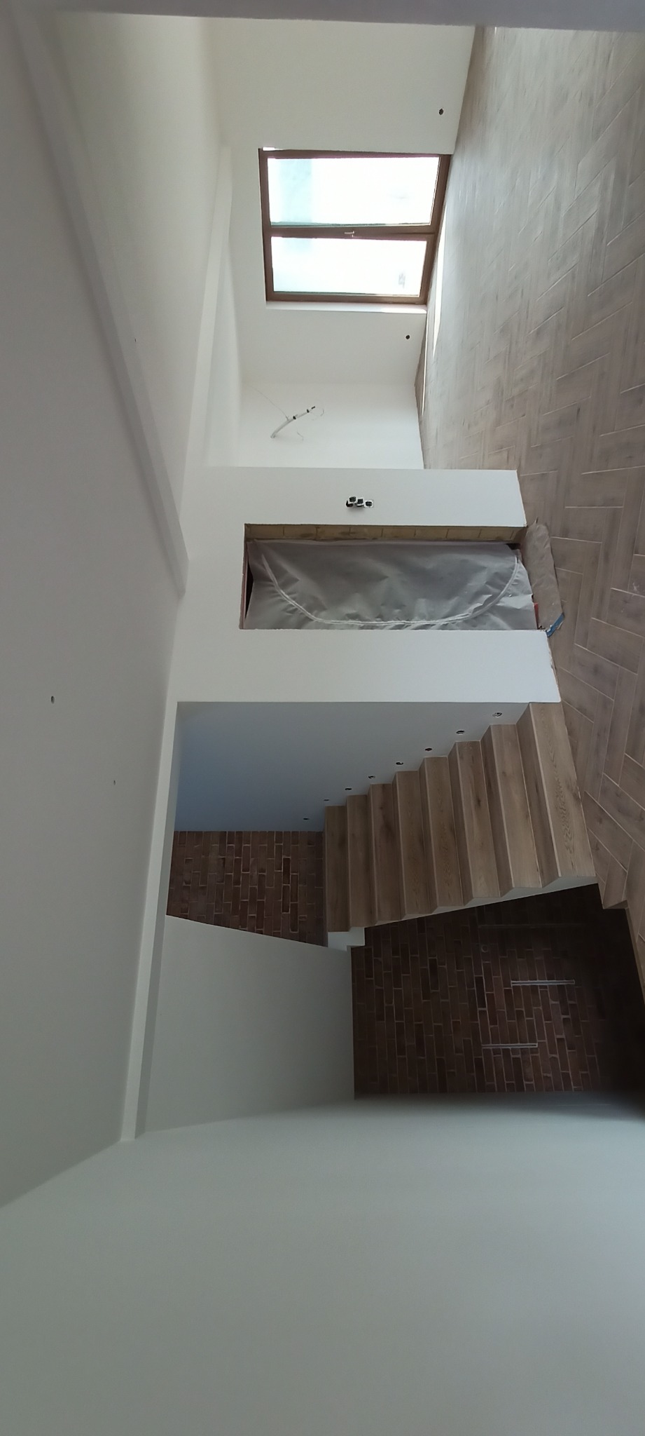 Nowoczesne wykończenie wnętrza w Ełku: drewniane schody, parkiet ułożony w jodełkę, białe ściany i okno dachowe. Minimalistyczny design, wysoki standard.