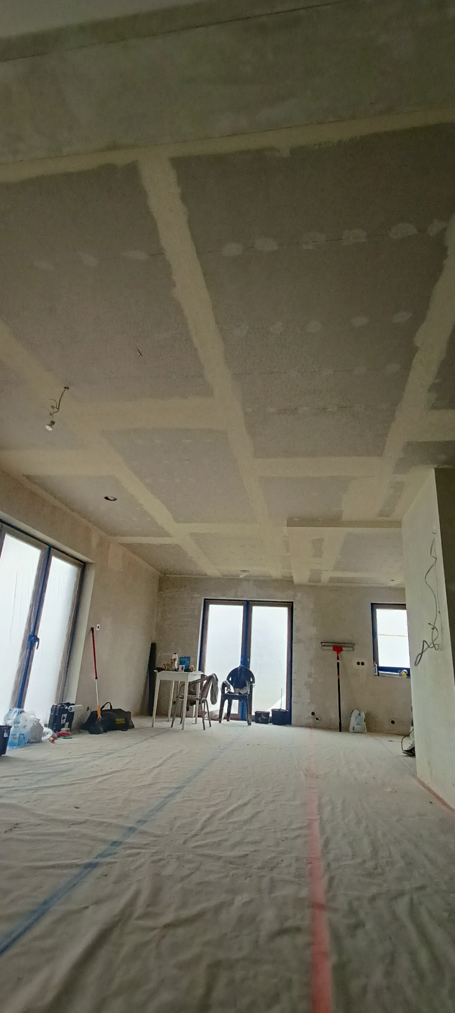 Pokój w trakcie prac wykończeniowych: zabezpieczona podłoga, ściany przygotowane do malowania, widoczne łączenia płyt gipsowo-kartonowych na suficie.