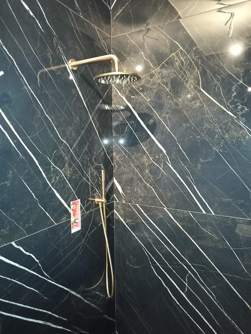 Złota armatura prysznicowa na tle czarnej ściany z marmurowym wzorem. Widoczny deszczownica i bateria. Na ścianie naklejka z oznaczeniami.