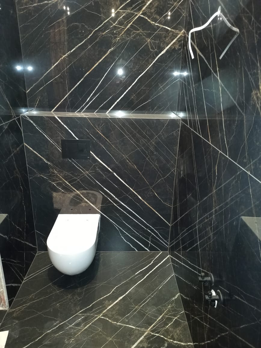 Elegancka toaleta w czarnym marmurze z białymi żyłami, podwieszana muszla klozetowa, czarny przycisk spłukujący, nowoczesne wykończenie łazienki.