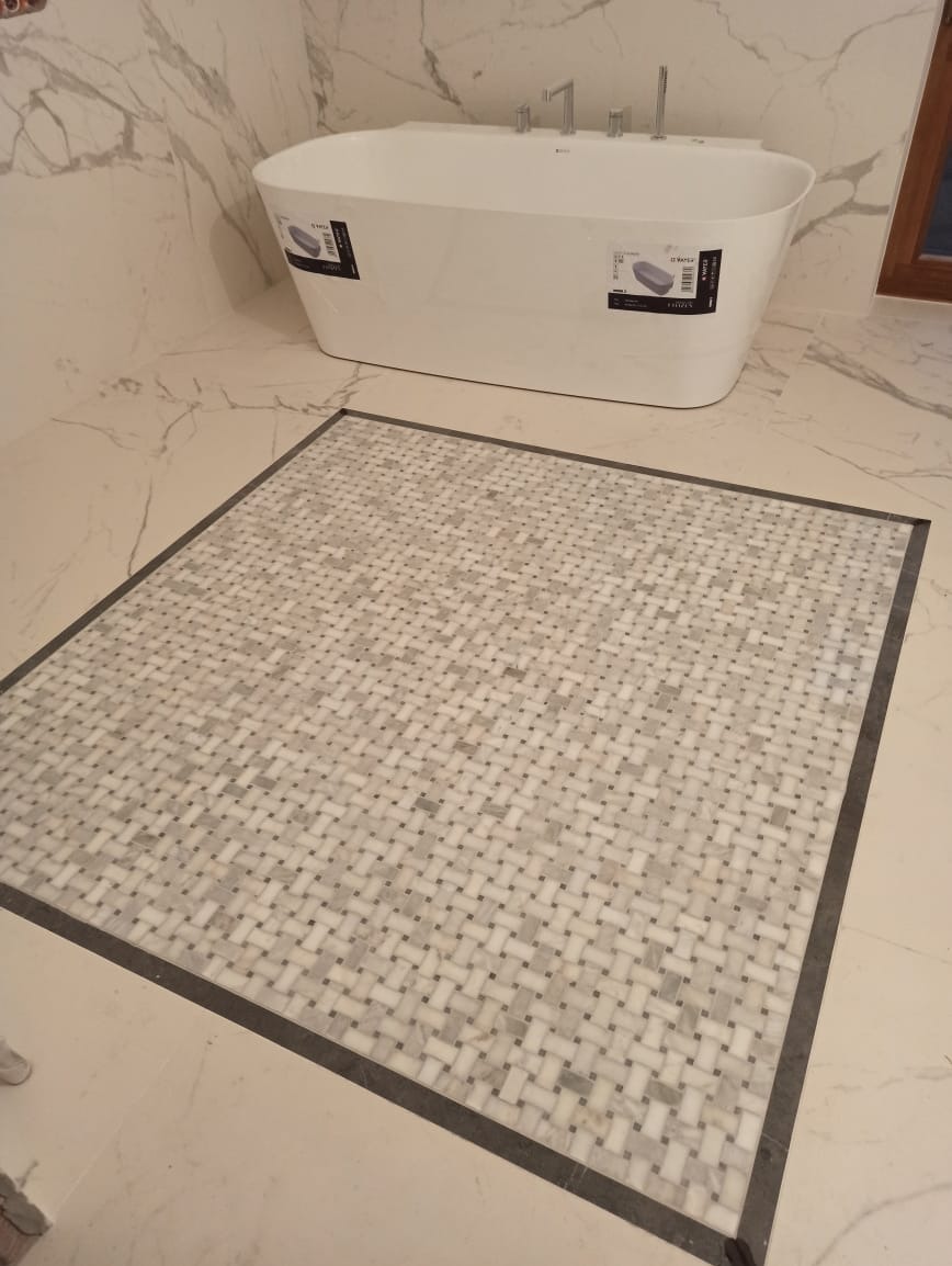 Nowoczesna łazienka z białą wanną wolnostojącą i dekoracyjną mozaiką podłogową w odcieniach bieli i szarości, otoczoną ciemnoszarą ramą.