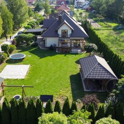 Bonus Nieruchomości - Widok z lotu ptaka na dom z ogrodem, gdzie widać trampolinę, plac zabaw, altankę i zadbany trawnik. Widoczne inne domy w oddali, słoneczny dzień.