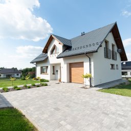 Bonus Nieruchomości - Nowoczesny dom jednorodzinny z garażem i brukowanym podjazdem w Rzeszowie. Biała elewacja, grafitowy dach, zadbany ogród. Widok z przodu, słoneczny dzień.