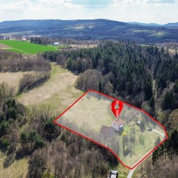 Bonus Nieruchomości - Widok z drona na dom z ogrodem, oznaczony czerwoną obwódką i pinezką lokalizacyjną, w otoczeniu lasów i pól. W tle pagórkowaty krajobraz.