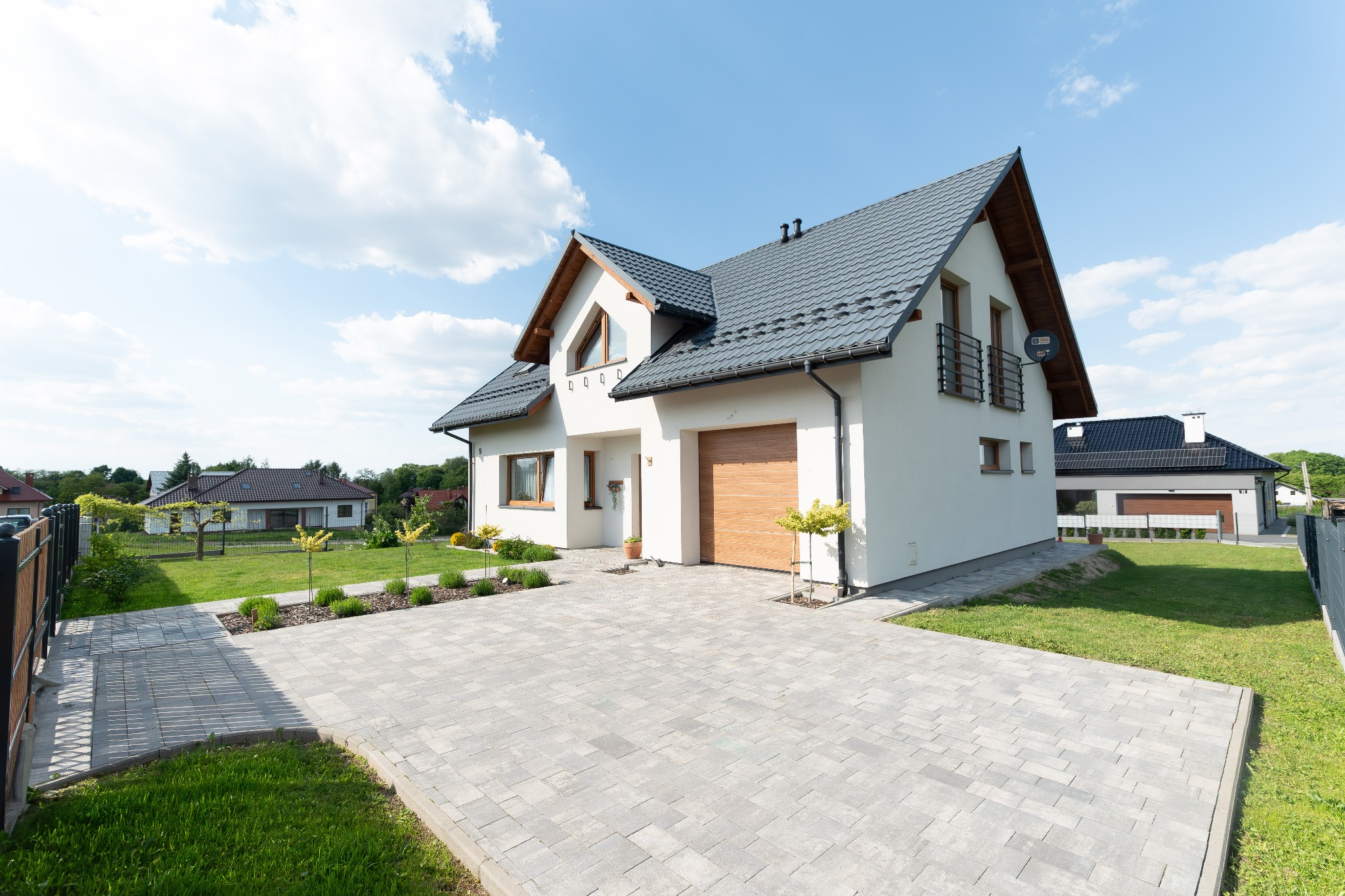 Nowoczesny dom jednorodzinny z garażem i brukowanym podjazdem w Rzeszowie. Biała elewacja, grafitowy dach, zadbany ogród. Widok z przodu, słoneczny dzień.