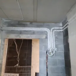 Surowe wnętrze w trakcie prac wykończeniowych: widoczne kable elektryczne prowadzone po ścianach z bloczków betonowych i suficie, z datą i godziną na dole kadru.