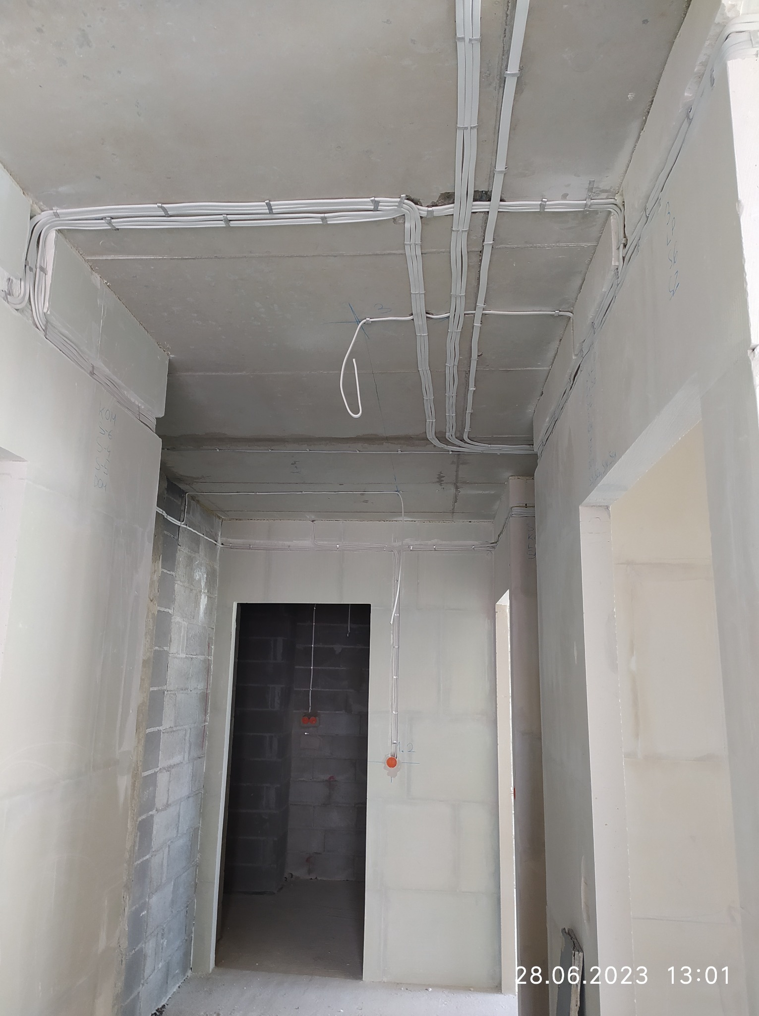 Rozprowadzone kable elektryczne pod sufitem w surowym wnętrzu, widoczne koryta kablowe i punkty instalacyjne na ścianach z pustaków.