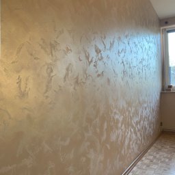 Proppo4k - Ściana w pokoju z dekoracyjną, beżowo-srebrną strukturą, widoczny fragment parkietu i okno.