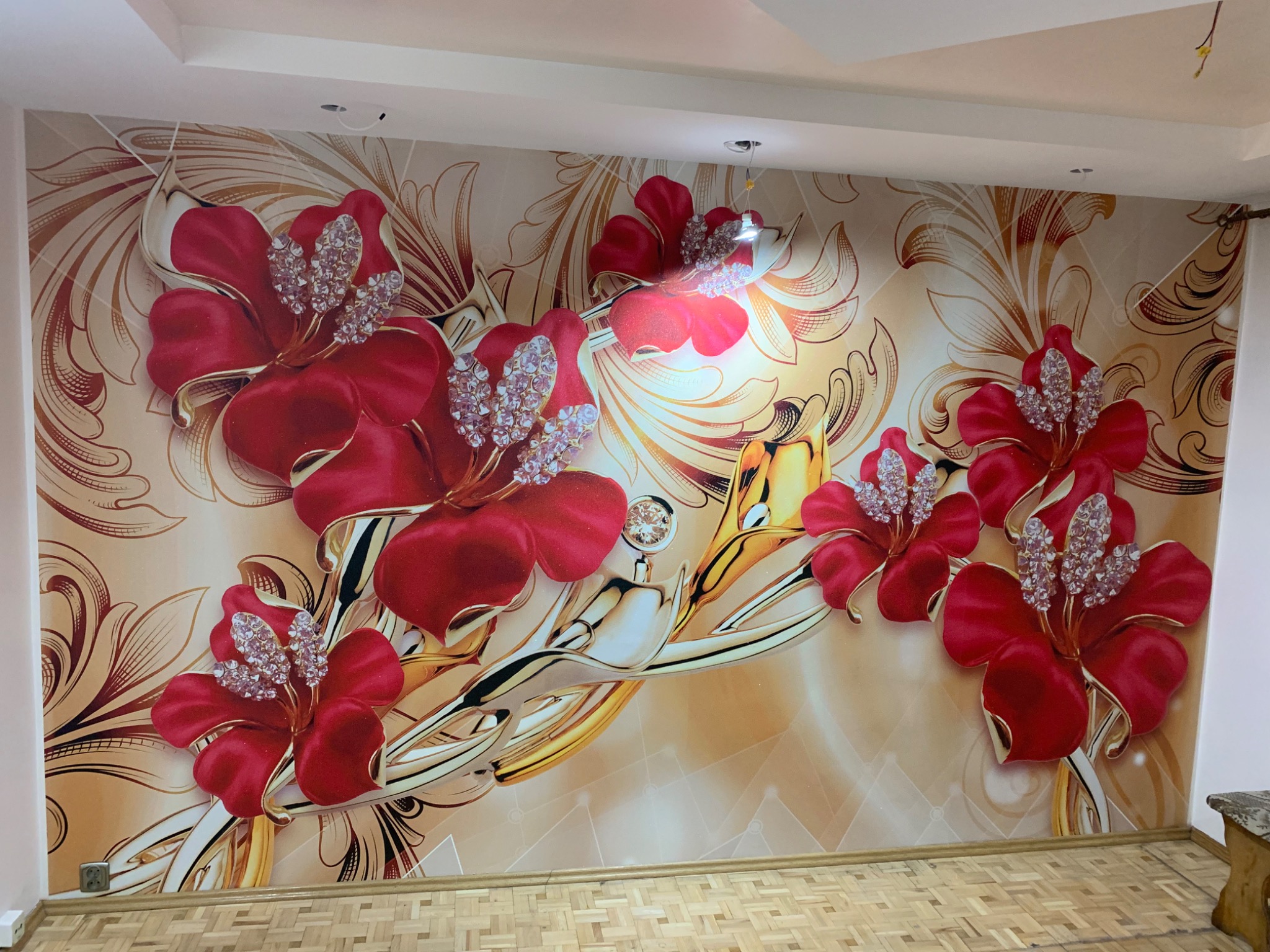 Fototapeta z motywem czerwonych kwiatów z kryształkami na beżowym tle z ornamentami, widok na ścianę i fragment parkietu.