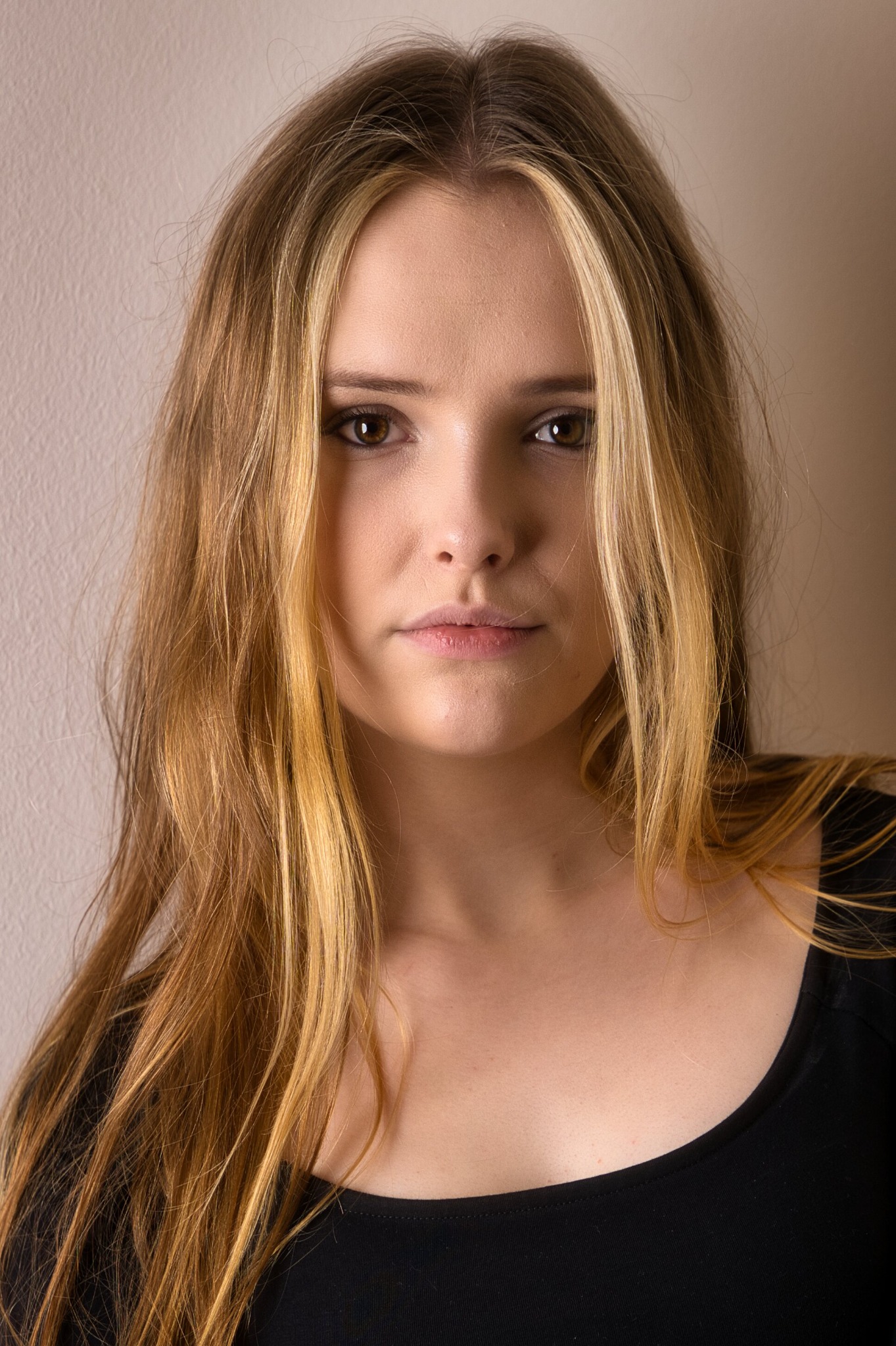 Portret młodej kobiety z długimi, blond włosami z pasemkami, ujęcie z bliska na neutralnym tle.