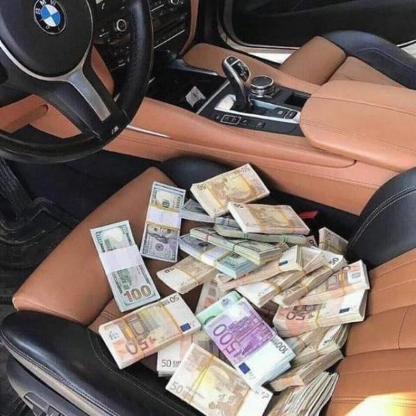 Stosy banknotów euro i dolarów leżące na skórzanym fotelu pasażera w luksusowym samochodzie z widoczną kierownicą i konsolą środkową.