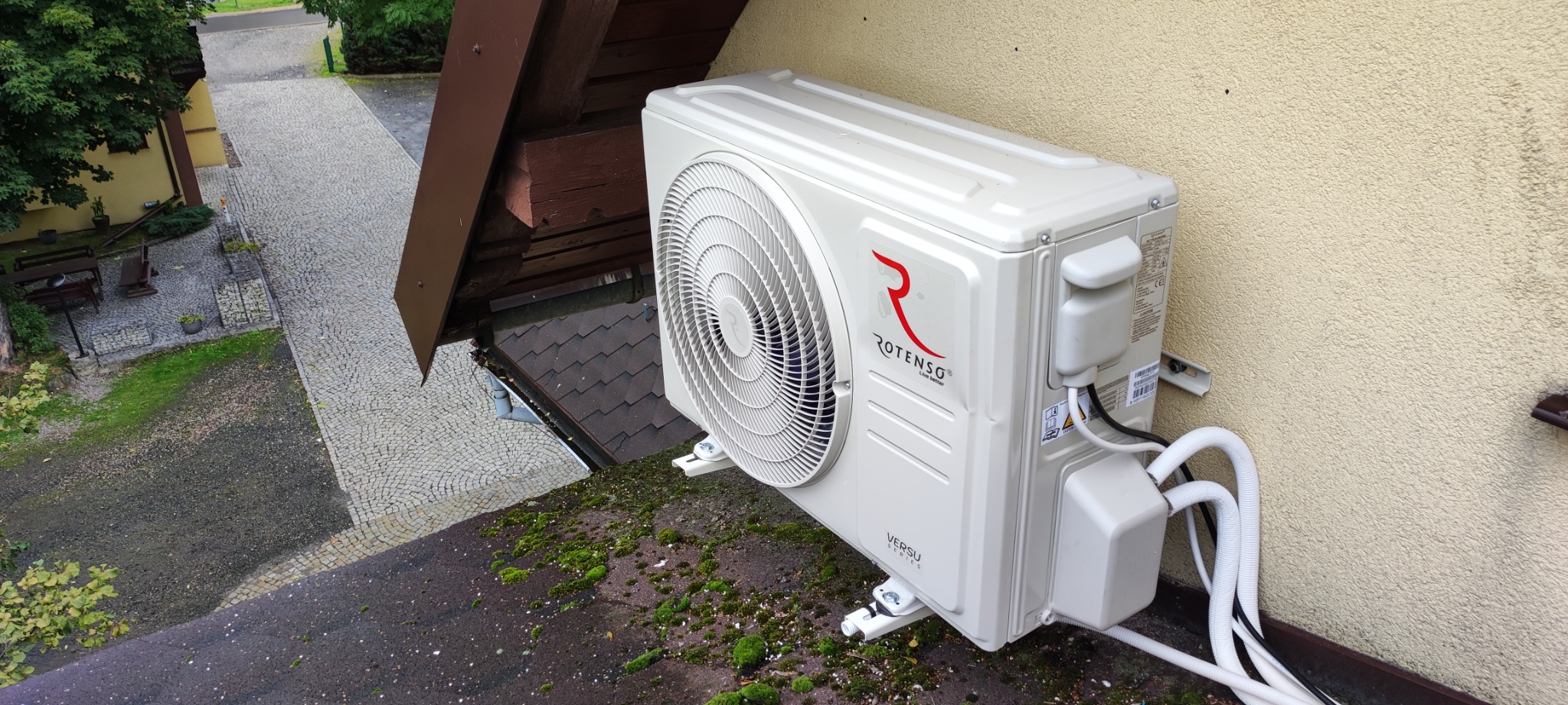 Zewnętrzna jednostka klimatyzacji Rotenso Versu Series zamontowana przy ścianie budynku w Jeleniej Górze, widok z góry na dach pokryty mchem.