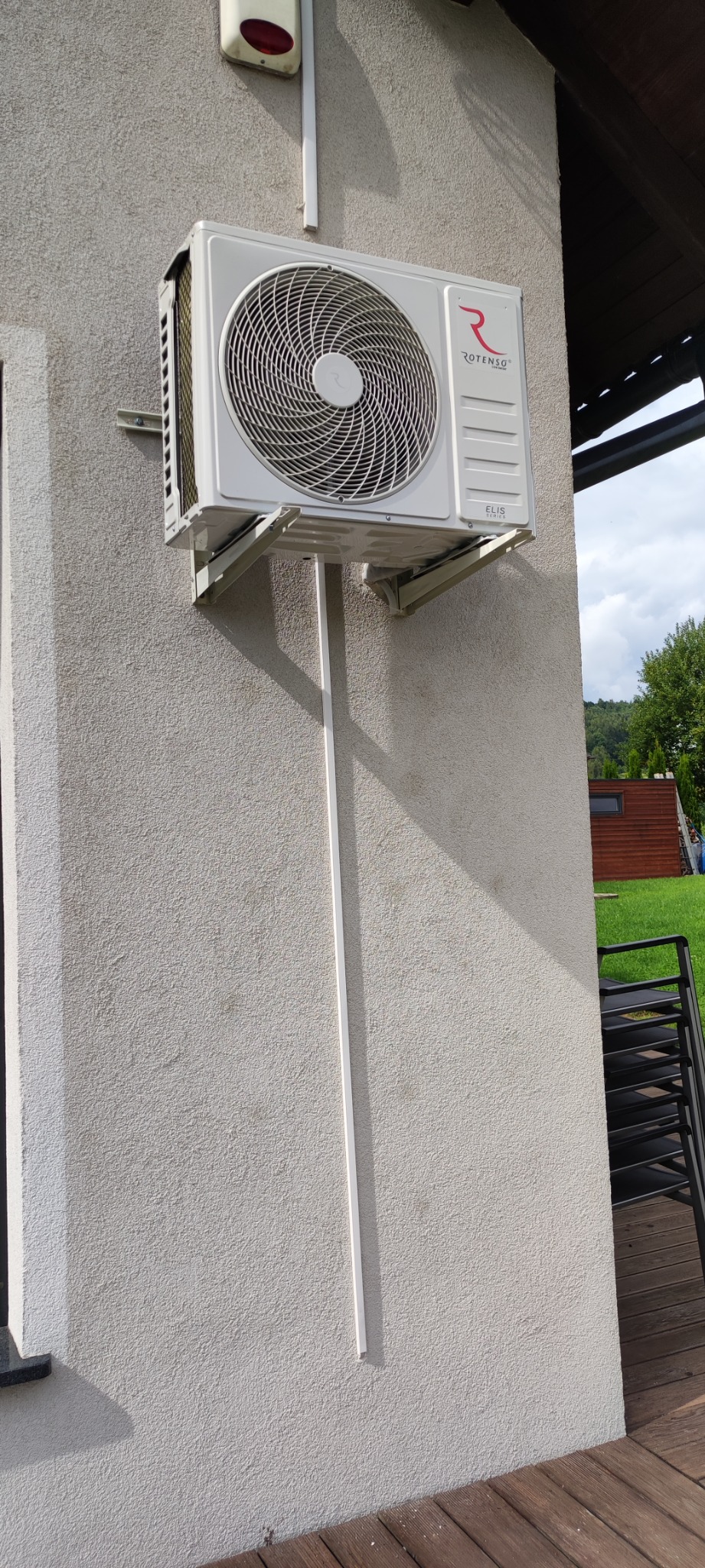 Zewnętrzna jednostka klimatyzacji Rotenso Elis Series zamontowana na ścianie domu z widoczną instalacją odprowadzającą skropliny w białej listwie.