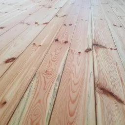 Jasna, drewniana podłoga z widocznym usłojeniem i sękami, ułożona z desek pod lekkim kątem.