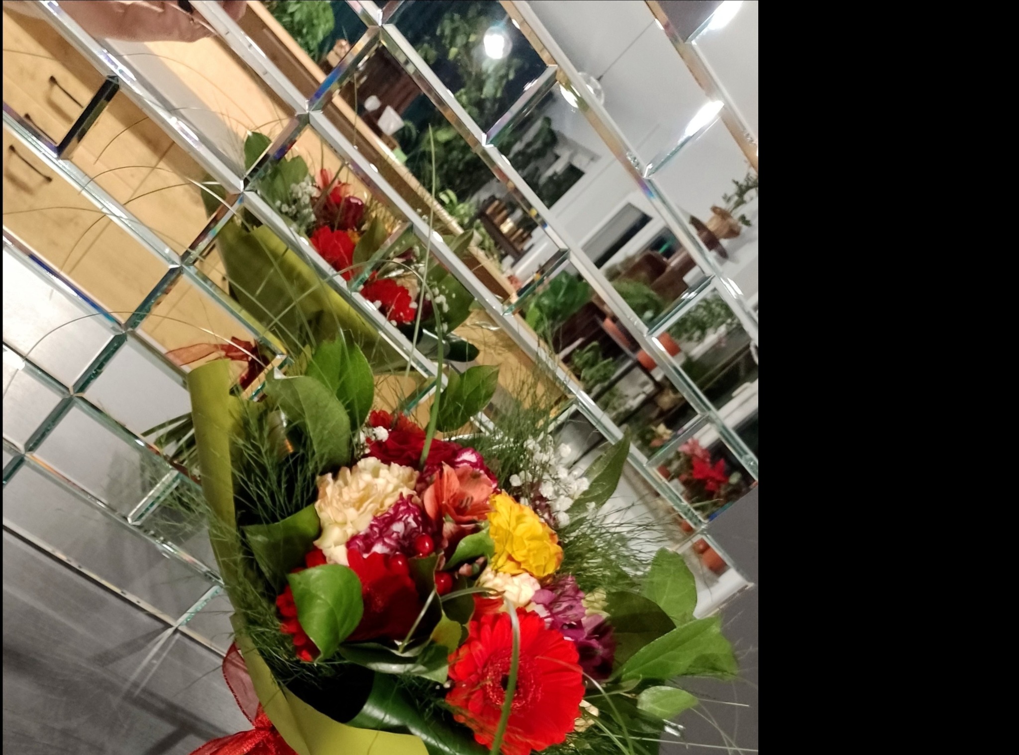 Bukiet mieszanych kwiatów w zielonym papierze, odbity w lustrzanej ścianie z kwadratowych płytek.