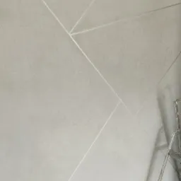 Jasnoszara ściana z dekoracyjnymi, srebrnymi liniami tworzącymi geometryczny wzór, drabina oparta o ścianę w prawym dolnym rogu.