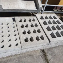 Betonowe płyty prefabrykowane z różnymi wzorami otworów: wypukłe półkule, owale, trójkąty, ułożone obok siebie na placu budowy.