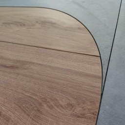 Pro-bud - Fragment podłogi z połączeniem paneli drewnopodobnych o zaokrąglonym kształcie i szarych płytek ceramicznych, widoczne fugi.