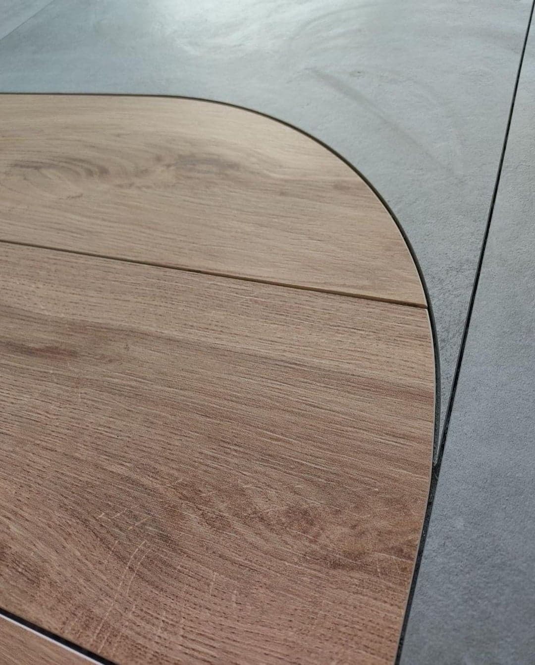 Fragment podłogi z połączeniem paneli drewnopodobnych o zaokrąglonym kształcie i szarych płytek ceramicznych, widoczne fugi.