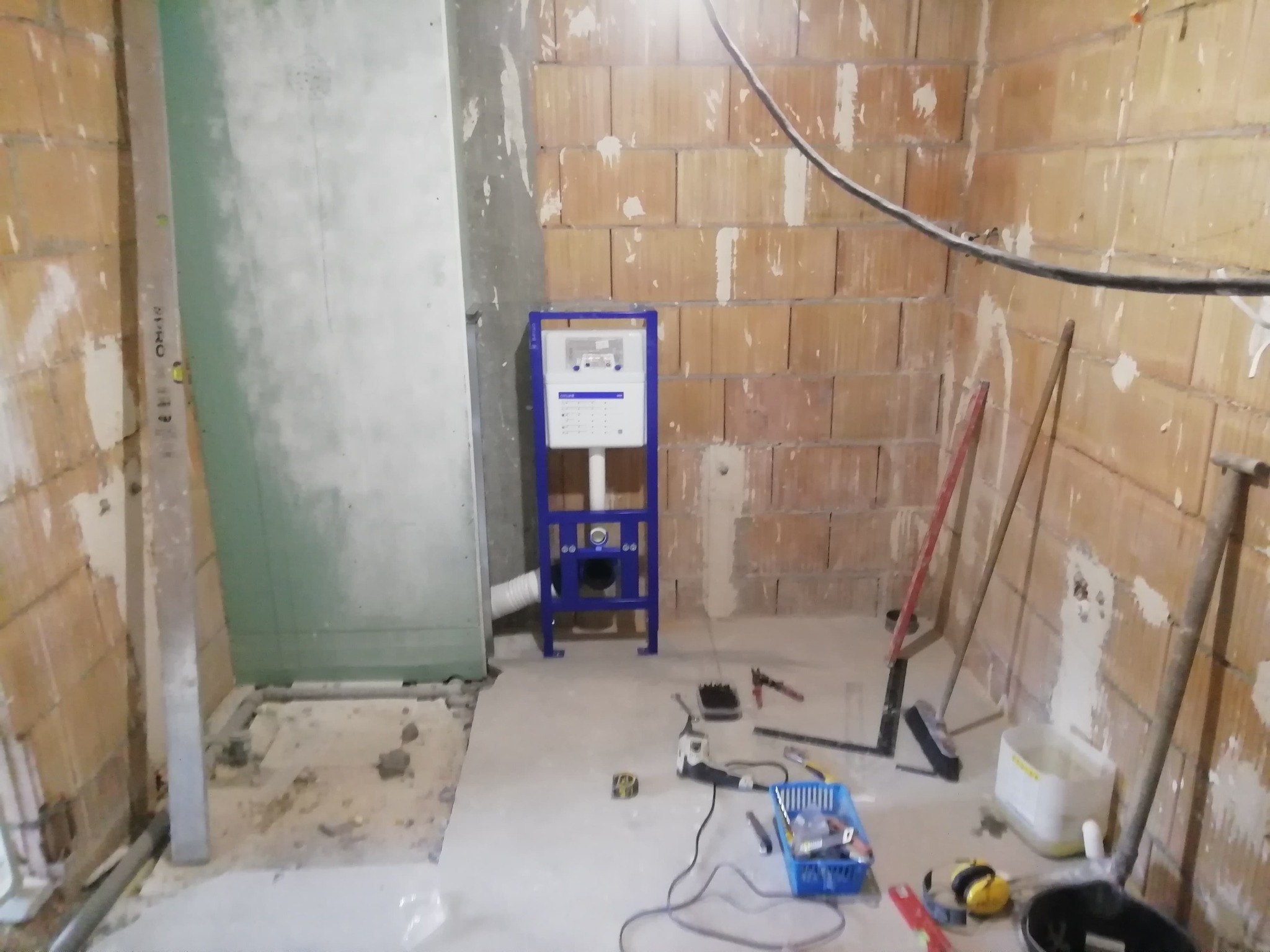 Montaż stelaża podtynkowego WC w surowej łazience z widocznymi narzędziami i instalacjami, ściany z cegły i płyty gipsowej przed wykończeniem.