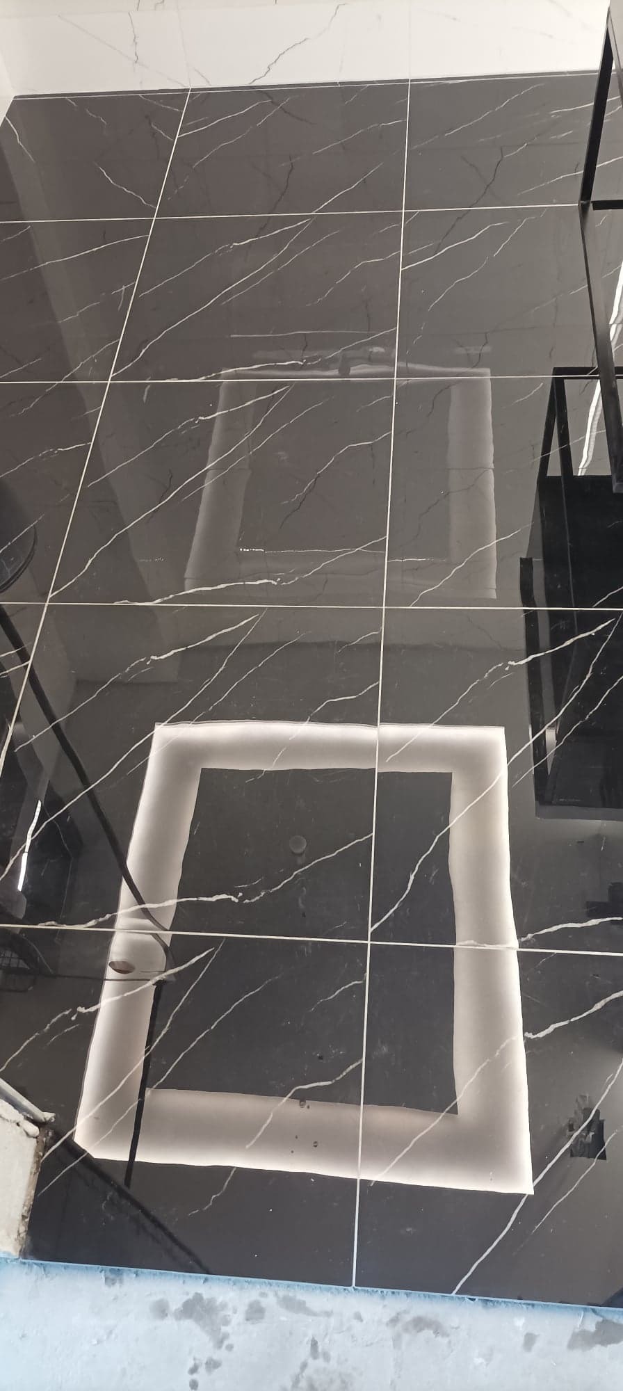 Czarne, błyszczące płytki podłogowe z białym marmurkowym wzorem i ledowym oświetleniem w kształcie kwadratu, widoczne fugi.