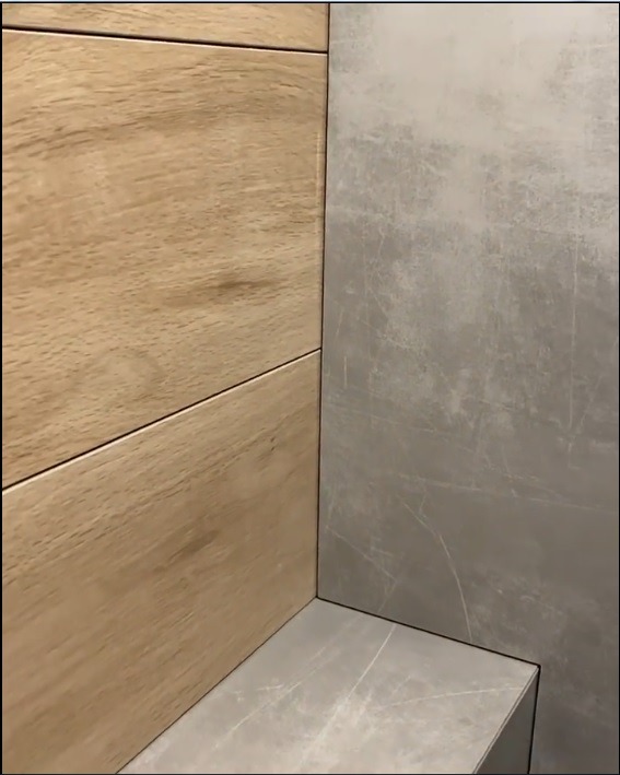 Detal narożnika łazienki wykończonego płytkami imitującymi drewno oraz szarym gresem z delikatnym wzorem żyłkowania.