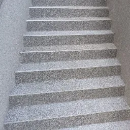 Zewnętrzne schody wejściowe do domu wykończone szarą, kamyczkową fakturą, z widocznymi aluminiowymi listwami zabezpieczającymi krawędzie stopni.