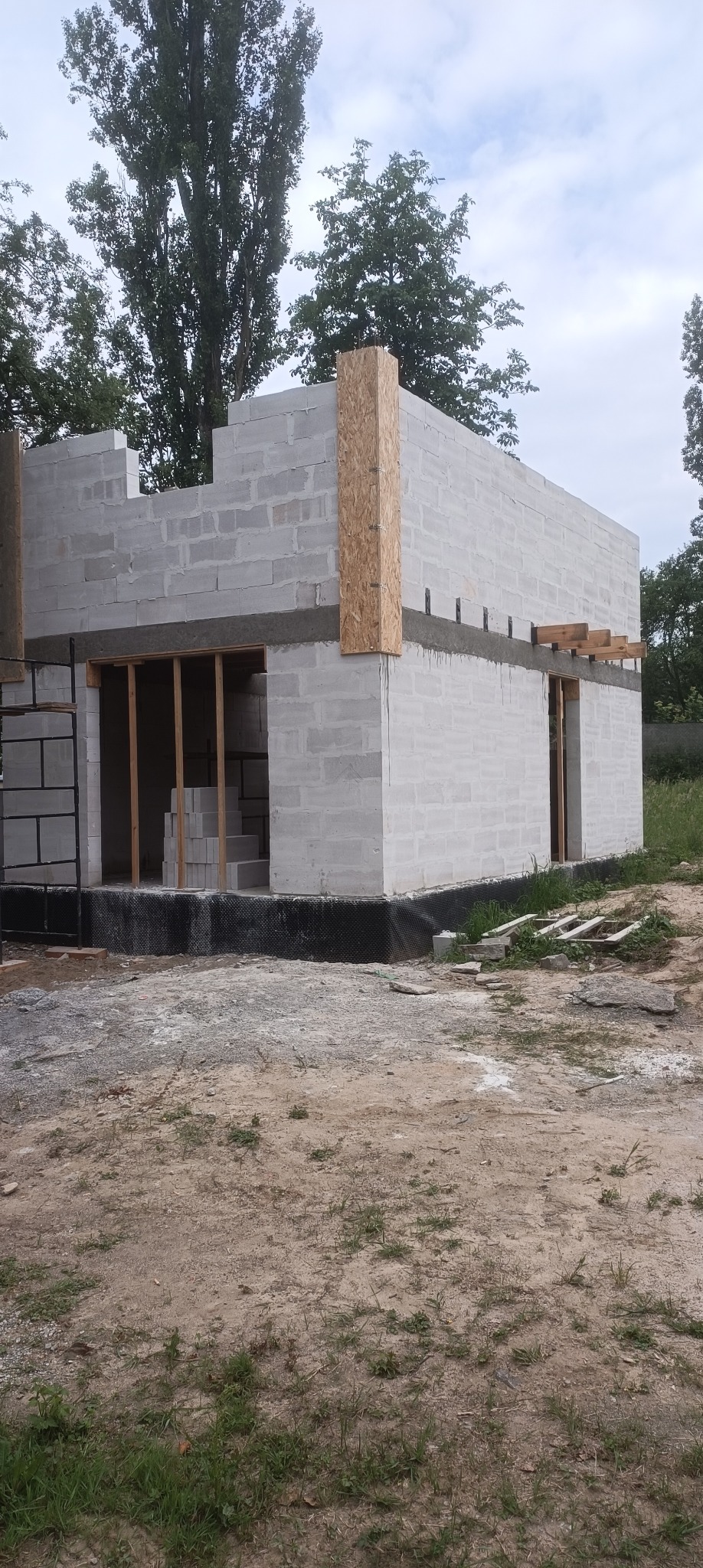 Wznoszenie ścian parterowego domu z bloczków betonu komórkowego, widoczne deskowanie otworów okiennych i drzwiowych oraz pionowe wzmocnienie narożnika płytą OSB.
