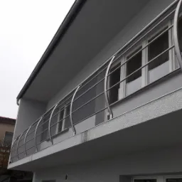 Balkon w Lublińcu z nowoczesną, metalową konstrukcją zabezpieczającą, widoczną z dołu, na tle pochmurnego nieba.