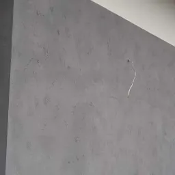 Szara ściana z efektem dekoracyjnym, widoczny fragment białego sufitu i wystający kabel elektryczny ze ściany.