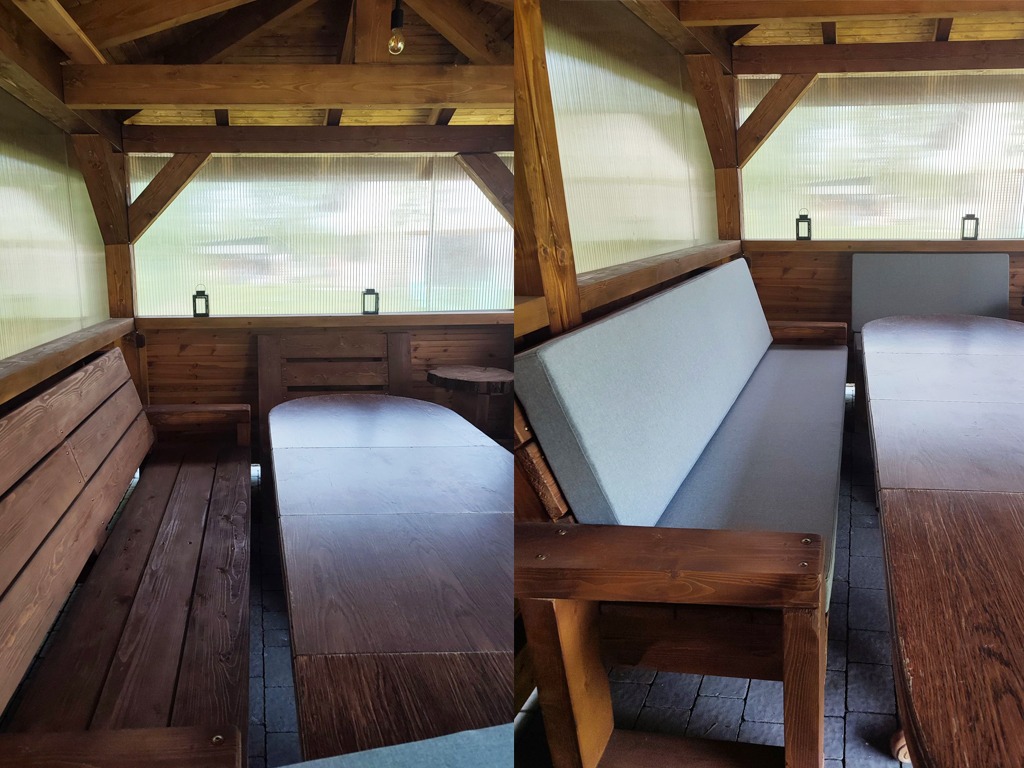 Wnętrze drewnianej altany z tapicerowanymi siedziskami w szarym kolorze i rozkładanym stołem z ciemnego drewna.