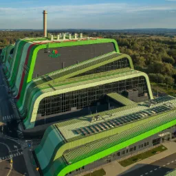 Widok z lotu ptaka na nowoczesną, ekologiczną spalarnię odpadów z panelami słonecznymi na dachu, otoczoną zielenią i drogami dojazdowymi.