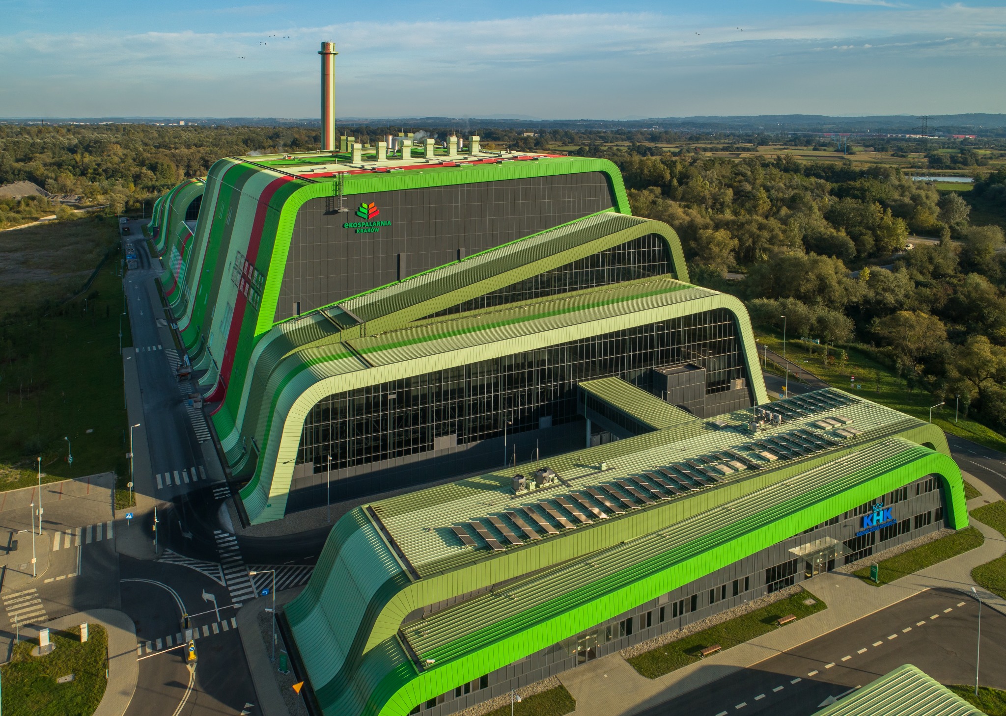 Widok z lotu ptaka na nowoczesną, ekologiczną spalarnię odpadów z panelami słonecznymi na dachu, otoczoną zielenią i drogami dojazdowymi.