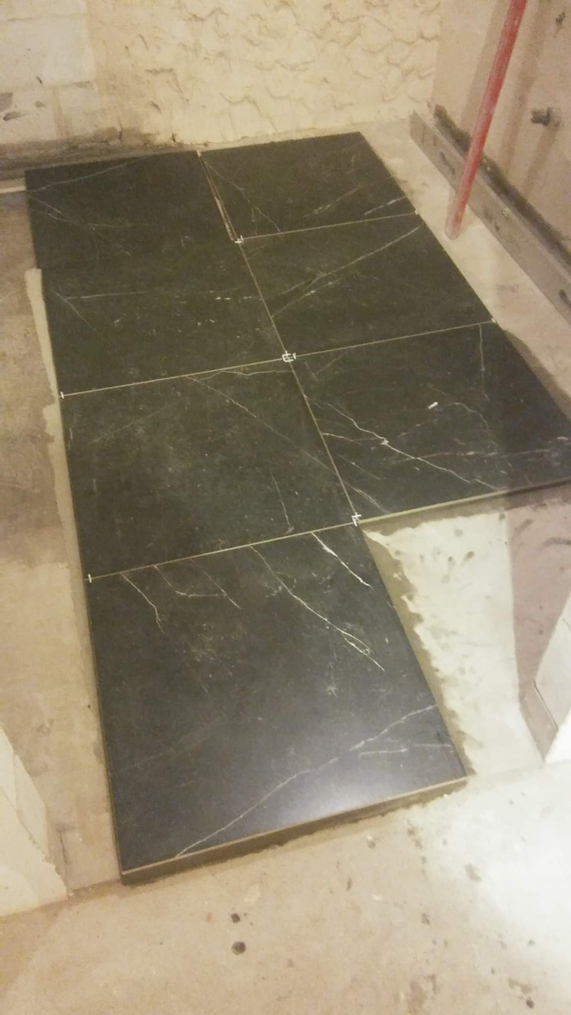 Ciemne płytki podłogowe z białym wzorem żyłkowym, ułożone na kleju z krzyżykami dystansowymi, w trakcie prac wykończeniowych w pomieszczeniu.