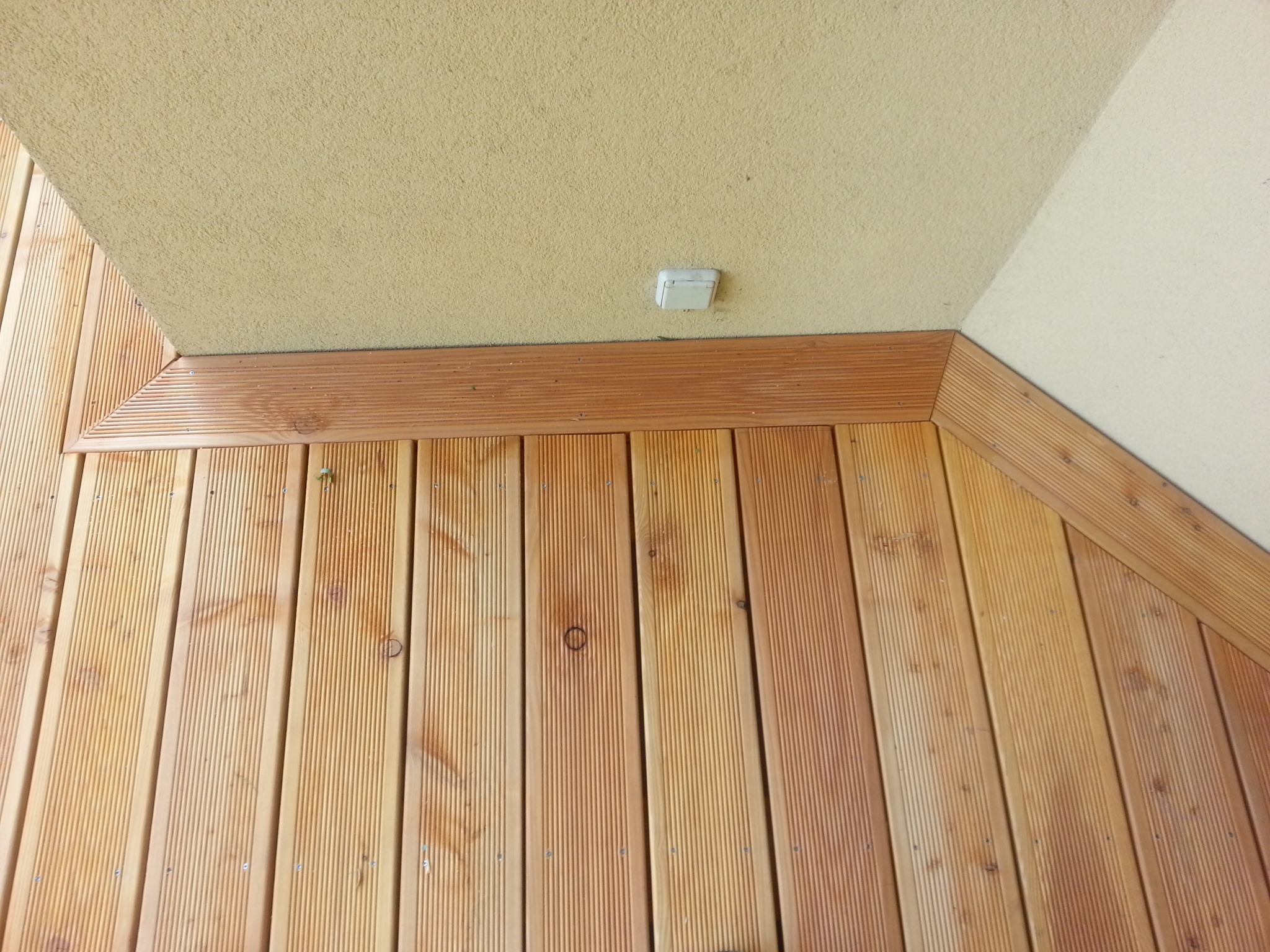 Drewniana boazeria ułożona pod kątem, z widoczną listwą wykończeniową i fragmentem sufitu z lampą