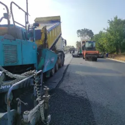 Asfaltowanie drogi w Krzycko Wielkie: Widok na rozściełacz asfaltu, ciężarówkę z wywrotem i walec drogowego podczas układania nowej nawierzchni.