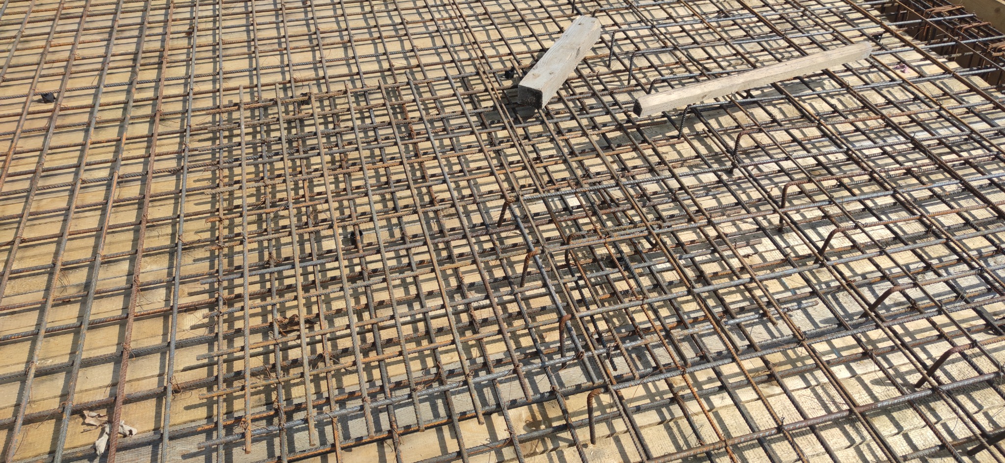 Zbrojenie z prętów stalowych ułożone na deskowaniu, przygotowane do wylania betonu na budowie domu.