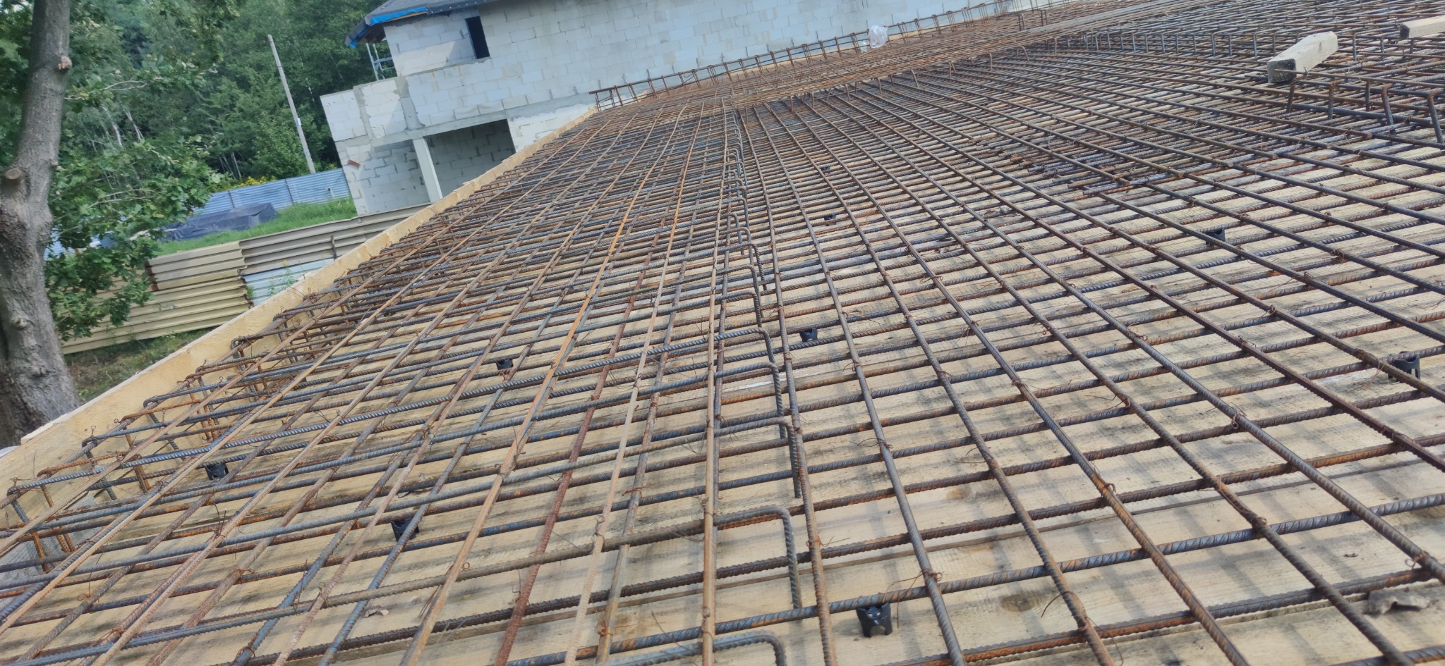 Zbrojenie płyty fundamentowej domu jednorodzinnego z widoczną siatką z prętów stalowych i dystansami z tworzywa sztucznego.
