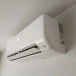 Biała jednostka wewnętrzna klimatyzacji marki Revio zamontowana na ścianie w Legnickim Polu, widoczny wyświetlacz z temperaturą 22 stopnie Celsjusza oraz naklejka z ostrzeżeniami.