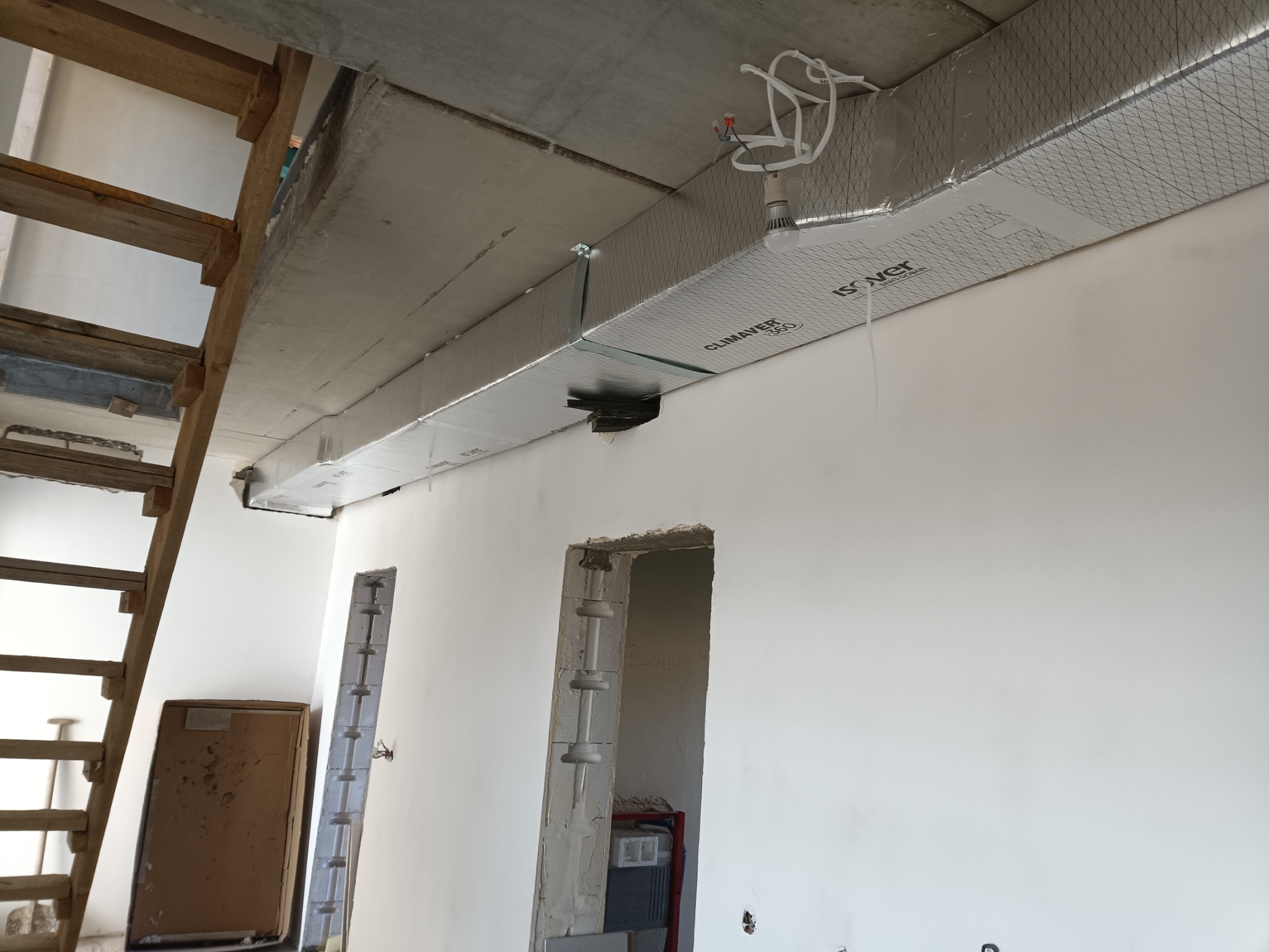 Montaż izolowanego kanału wentylacyjnego Climaver Isover 360 pod betonowym sufitem w surowym wnętrzu, widoczne fragmenty drewnianych schodów i niedokończone otwory w ścianie.