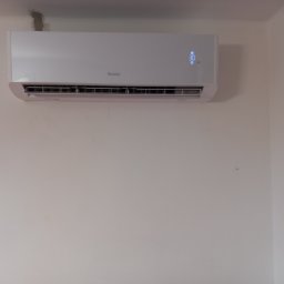 P-bud Kalicki Przemysław - Biały klimatyzator marki Gree zamontowany na ścianie, wyświetlający temperaturę 30 stopni, widoczne ślady po naprawach na ścianie nad urządzeniem.