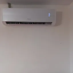 Biały klimatyzator marki Gree zamontowany na ścianie, wyświetlający temperaturę 30 stopni, widoczne ślady po naprawach na ścianie nad urządzeniem.